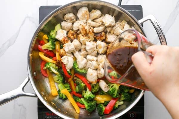 Hoisin sauce poured over stir fried chicken and veggies in a skillet.
