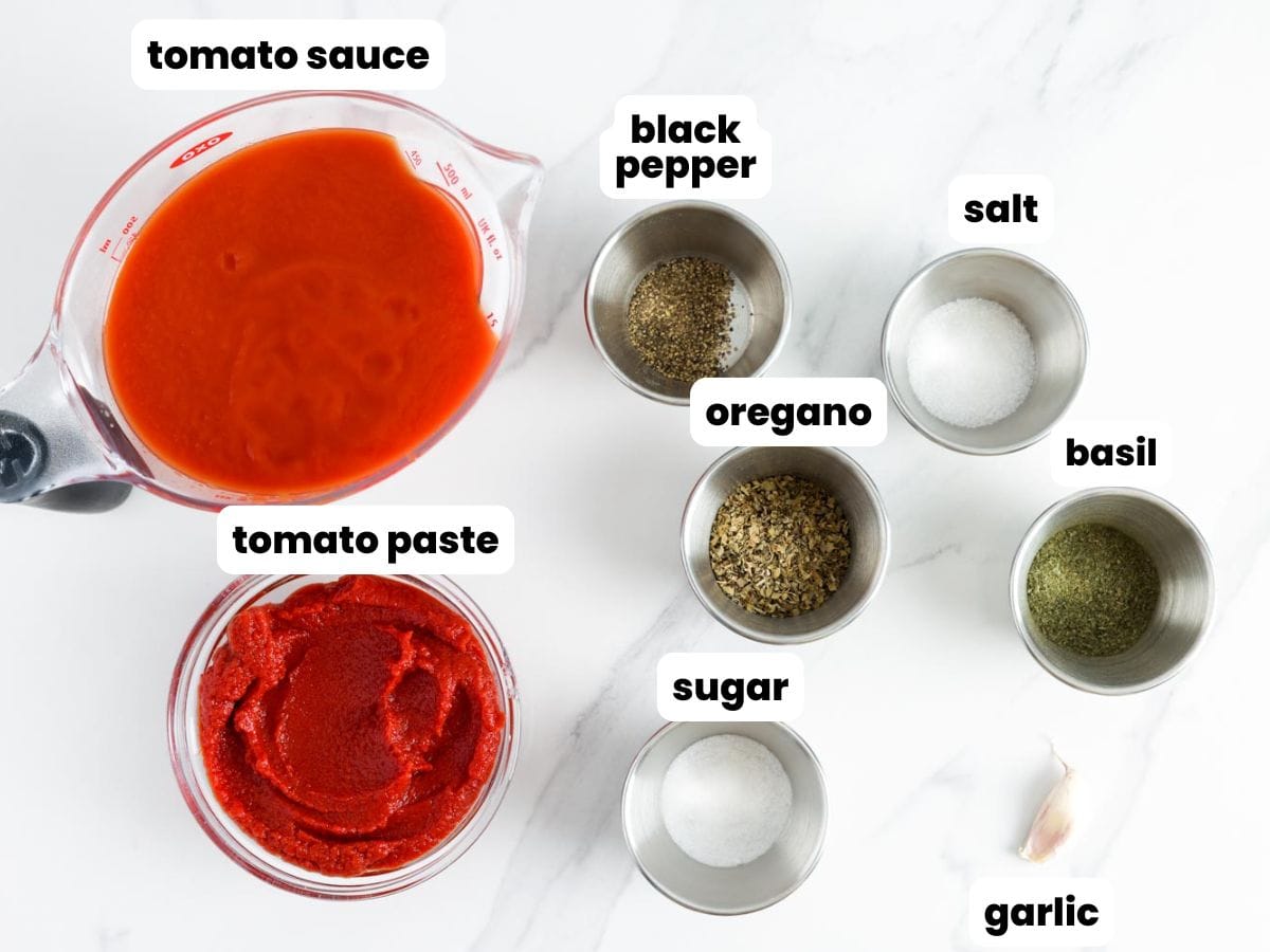Measured ingredients for homemade pizza sauce including tomato sauce, tomato paste, garlic, oregano, basil, sugar, salt, and black pepper displayed in bowls.