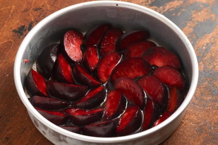 Quartered fresh plums arranged in a single layer over caramel sauce in a round cake pan.