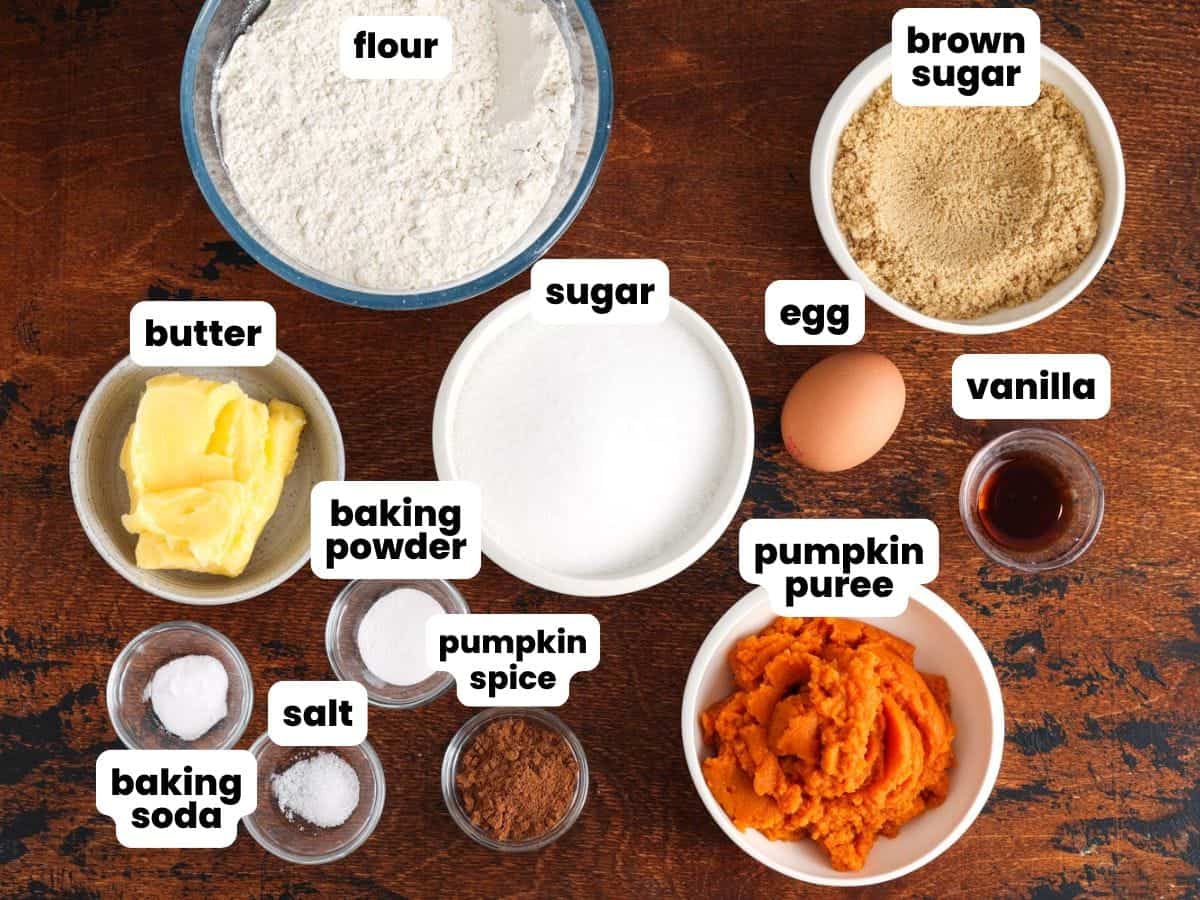 Ingredients needed to make pumpkin cookies including pumpkin puree, flour, sugar, butter, brown sugar, egg, vanilla, pumpkin spice, baking powder and soda, and salt.