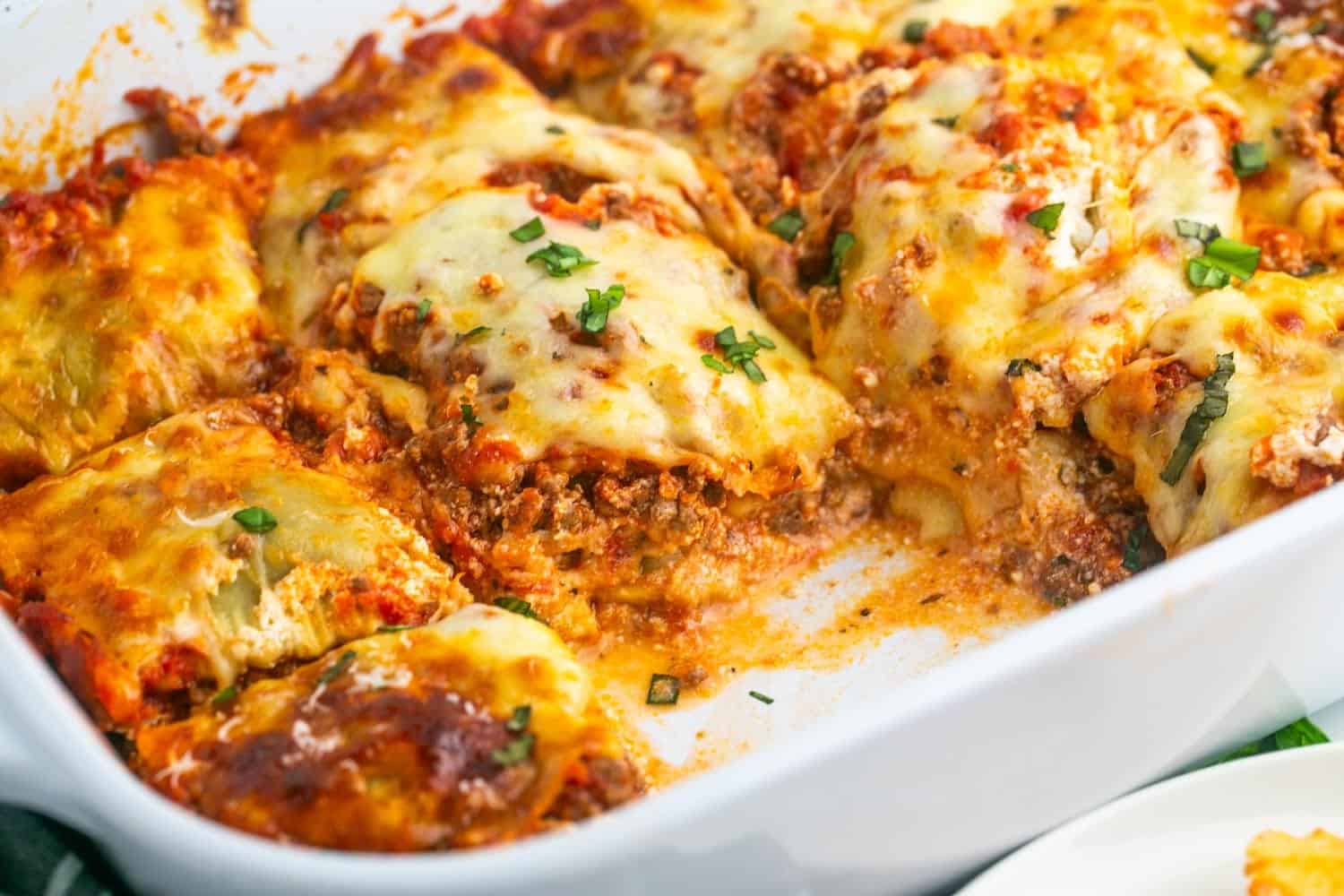 a casserole pan filled with lasagna made with ravioli. it's been cut into servings and one square is removed.