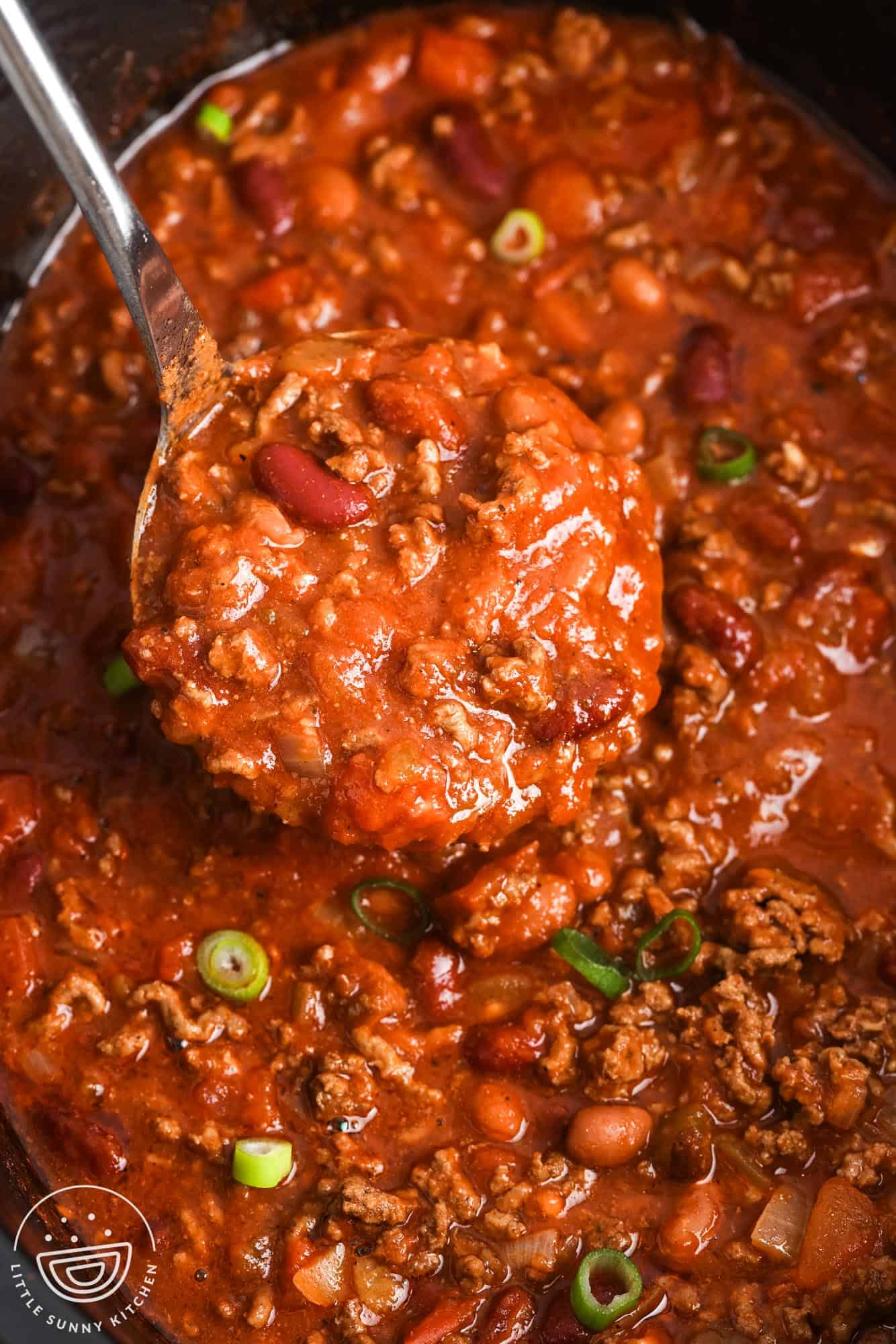 closeup of slow cooker beef chili in a crockpot. A ladle is holding up a serving.