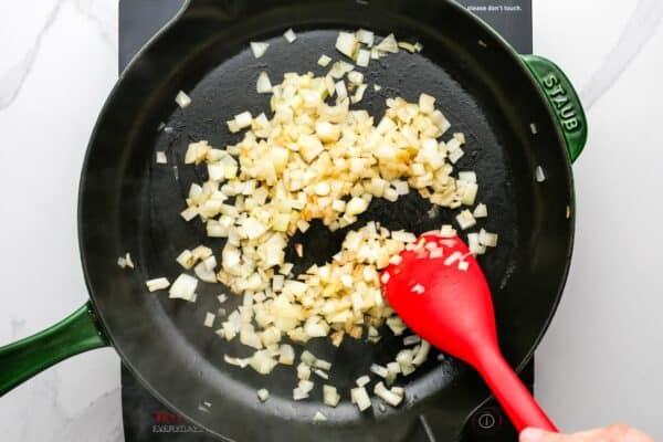 diced onions sauteing in a skillet, stirred with a red spoon.