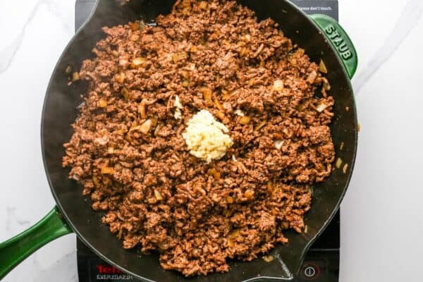 minced garlic added to a skillet of cooked ground beef and onions.
