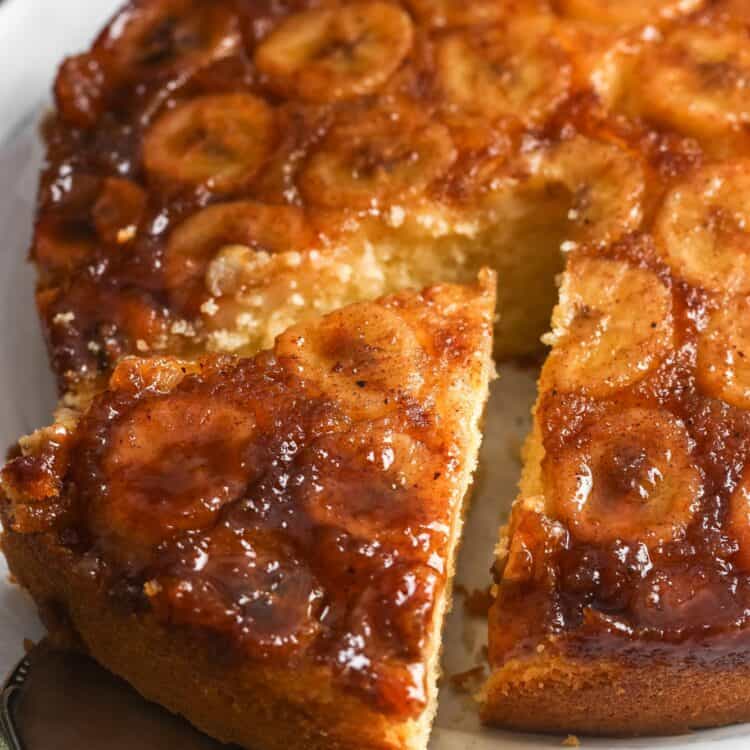 A cake server lifting a slice of banana upside down cake, with caramelized bananas glistening on top.