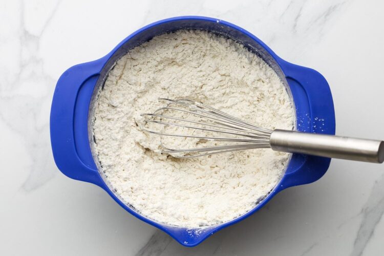 flour in a large blue mixing bowl, stirred with a whisk.