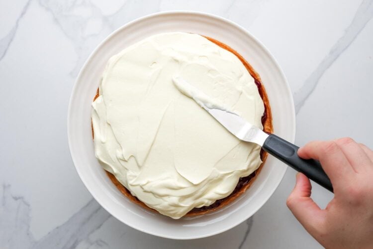 whipped cream spread over a victoria sponge cake on a plate.