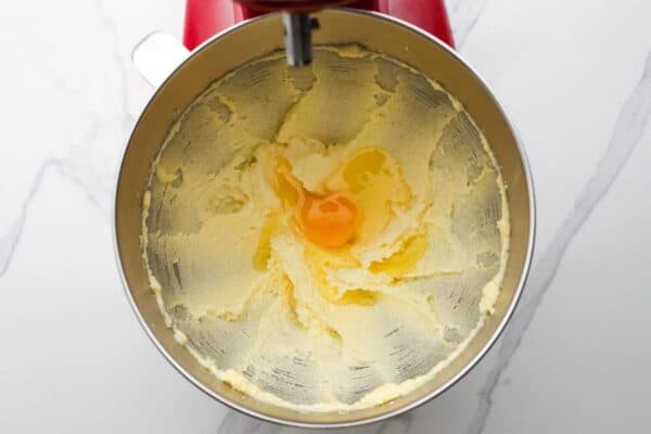 An egg added to creamed butter and sugar in the bowl of a stand mixer.