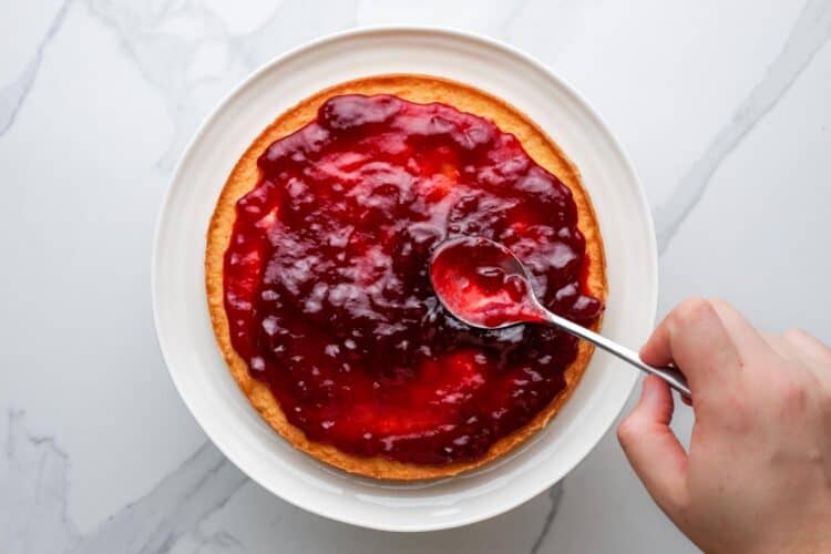 raspberry jam spread over a round layer of cake that is on a plate.