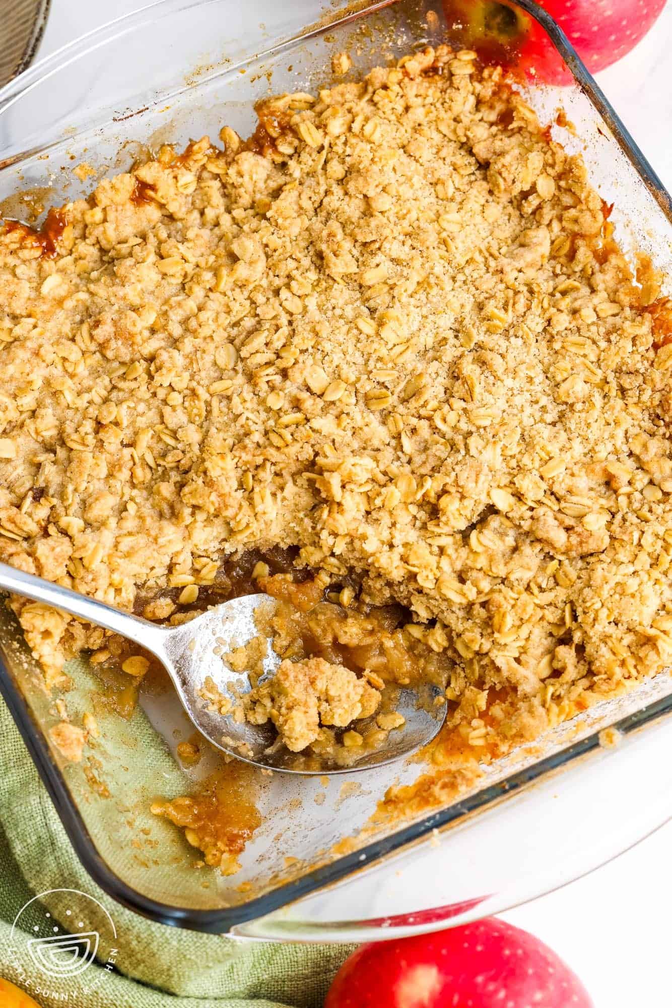 overhead view of a square pan of apple crisp with one serving removed with a large metal spoon.