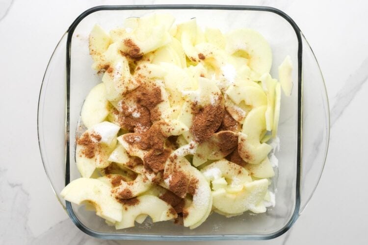 sliced apples in a square glass pan, topped with sugar and cinnamon.