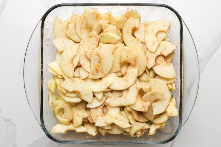 thinly sliced apples in a square glass pan, seasoned with cinnamon.