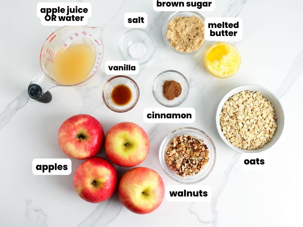Overhead view of ingredients for baked apples with oats, including apples, oats, walnuts, brown sugar, cinnamon, vanilla, salt, melted butter, and a measuring cup of apple juice or water, each labeled with text.