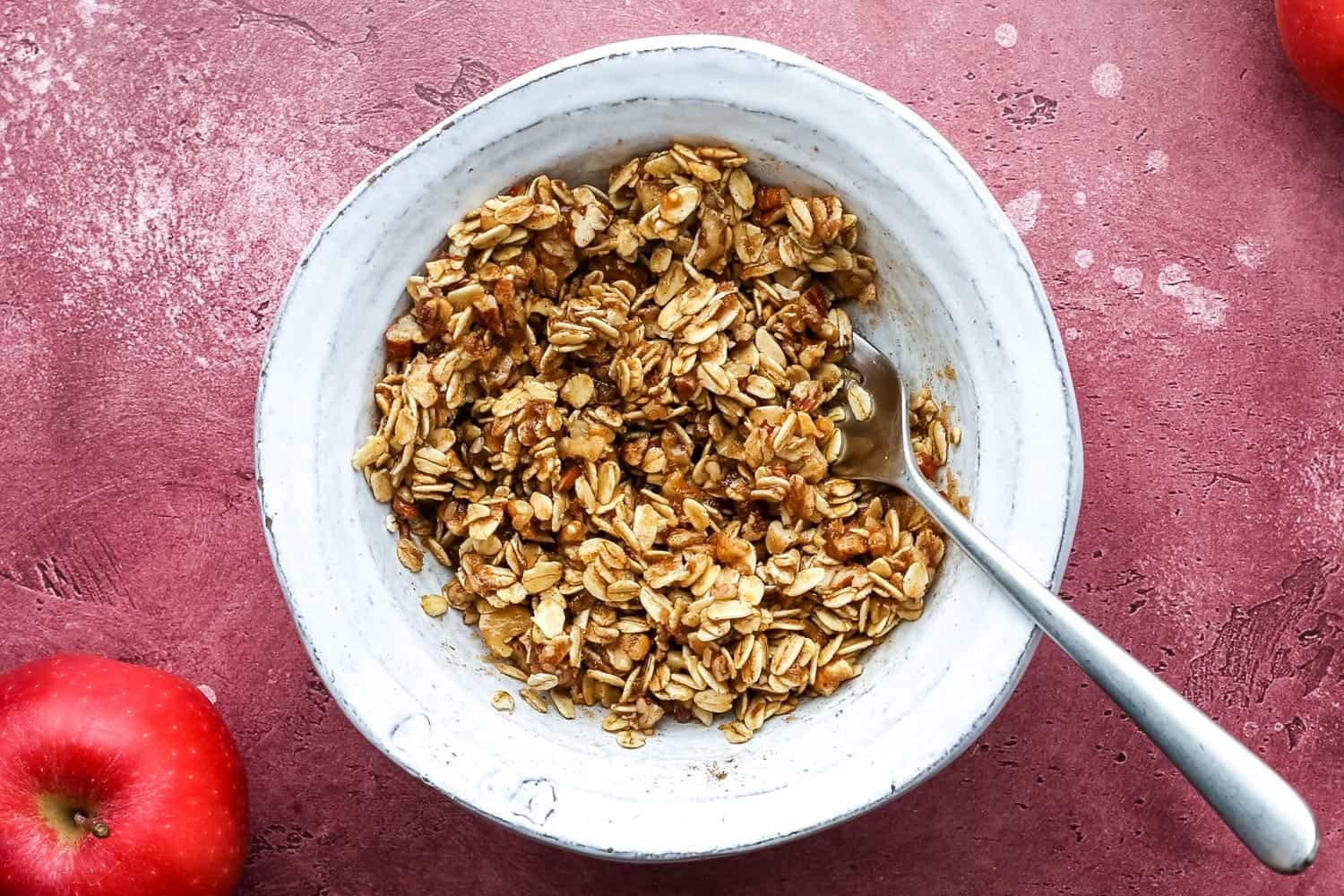 A white bowl filled with an oat, nut, and cinnamon mixture with a spoon inside.