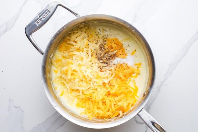 shredded cheeses added to a cream sauce in a saucepan. It's seasoned with black pepper.