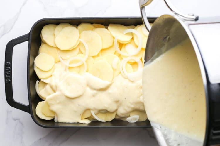 cheese sauce poured over sliced potatoes in a black baking dish.