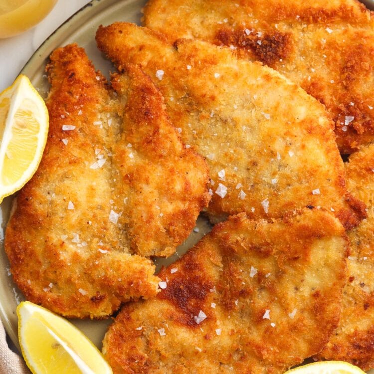 a platter of chicken milanese cutlets with lemon wedges on the side.