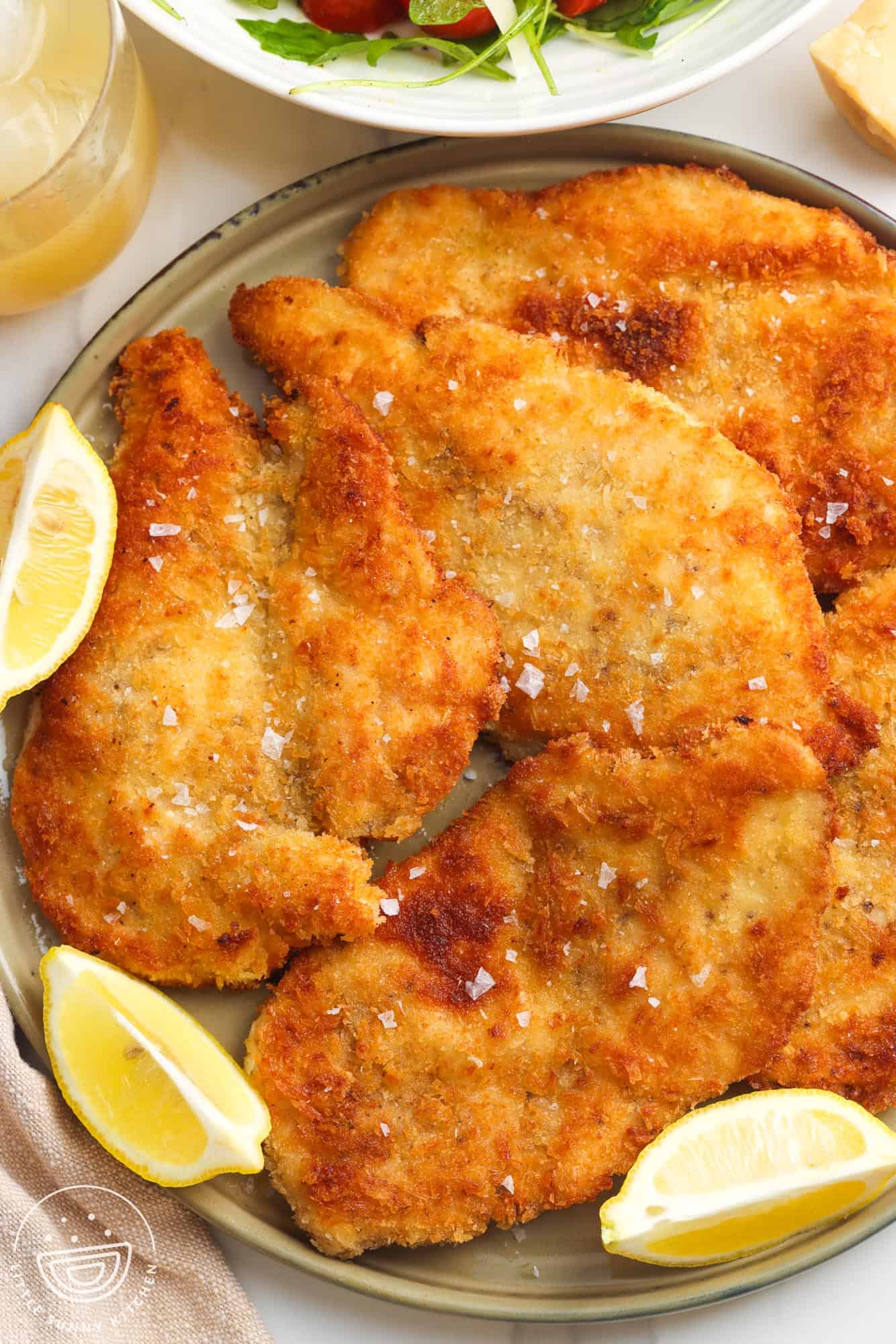 a platter of chicken milanese cutlets with lemon wedges on the side.