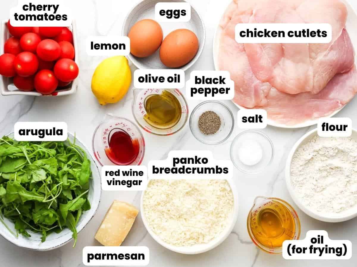 a plate of raw chicken cutlets next to small bowls of ingredients needed to make chicken milanese with arugula salad
