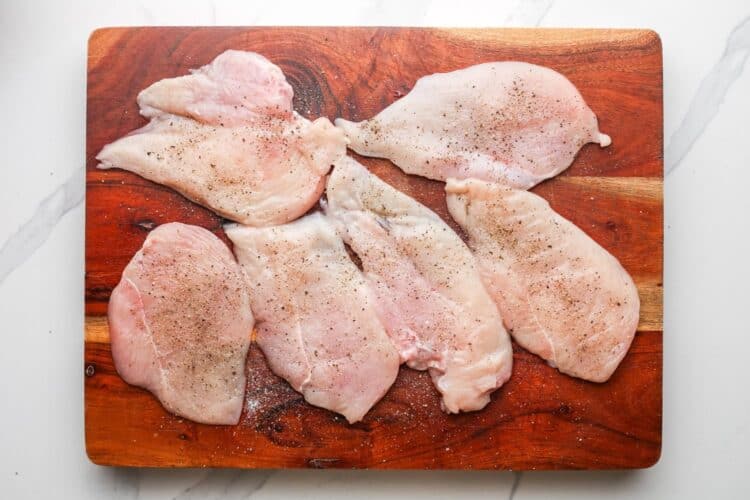 chicken cutlets on a wooden cutting board, seasoned with salt and pepper.