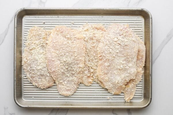 breaded chicken cutlets on a small metal sheet pan.