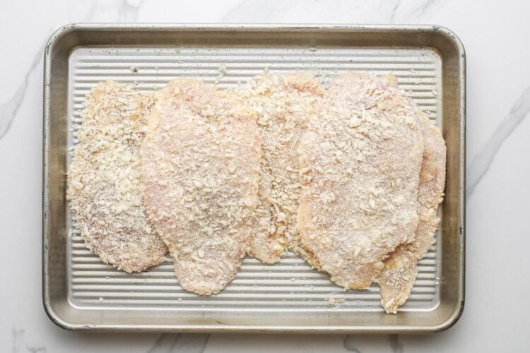 breaded chicken cutlets on a small metal sheet pan.