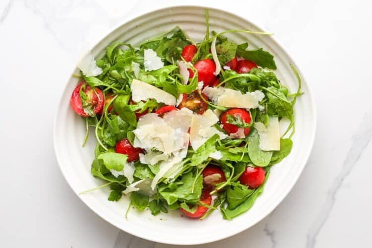 an arugula salad with shaved parmesan and halved cherry tomatoes.