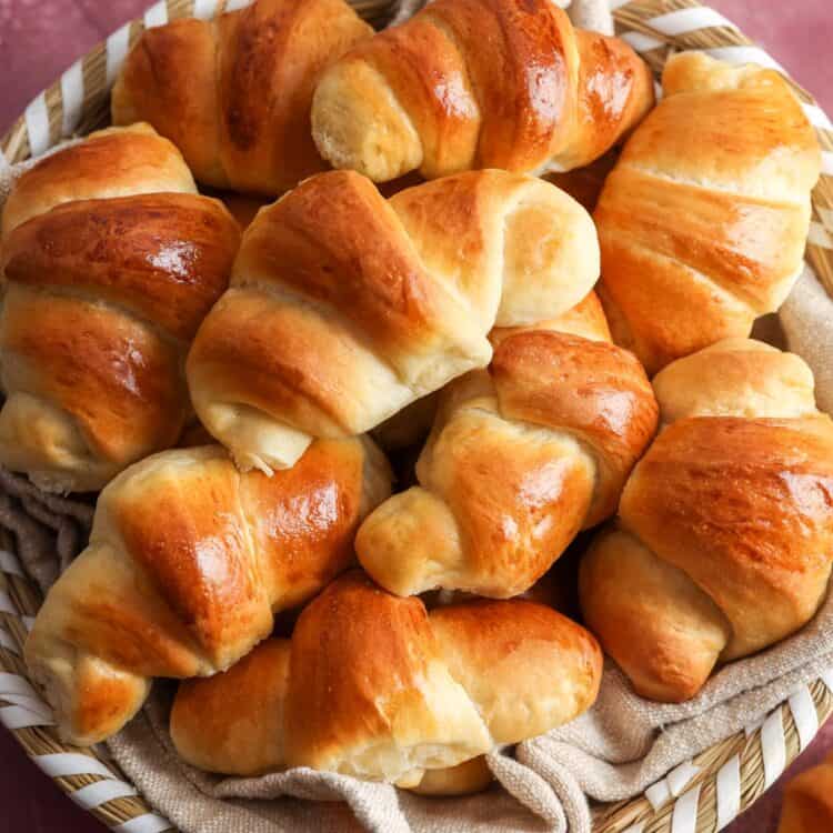 a basket lined with a tan cloth, filled with homemade crescent dinner rolls.
