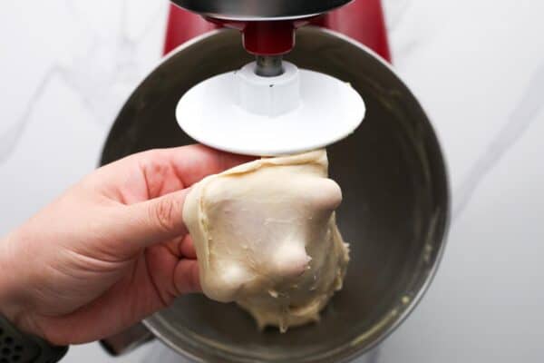 a hand picking up the dough for crescent rolls to show how it passes the windowpane test. It can be stretched and you can see through it.