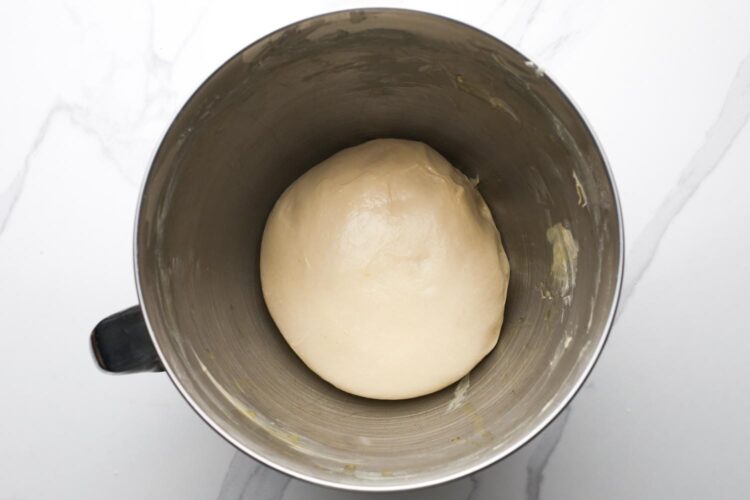 crescent roll dough before rising in a metal stand mixer bowl that is coated with butter.
