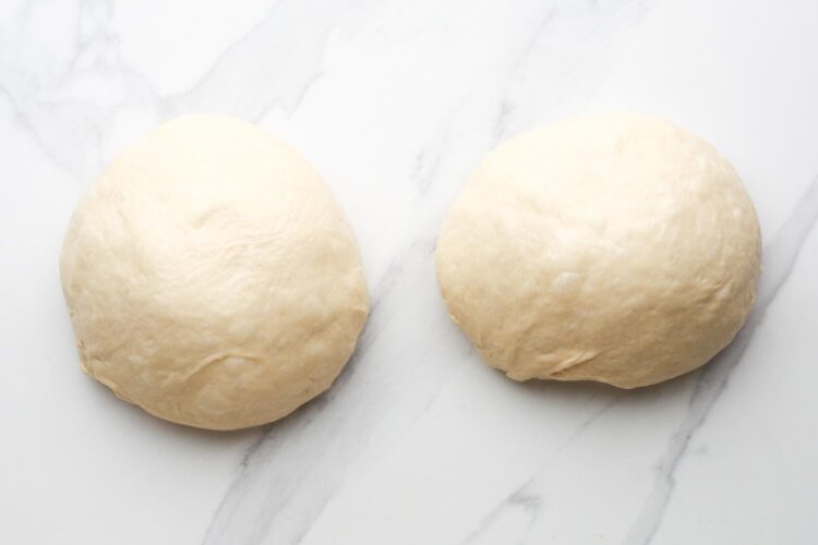 two balls of dough after rising, set on a marble counter.