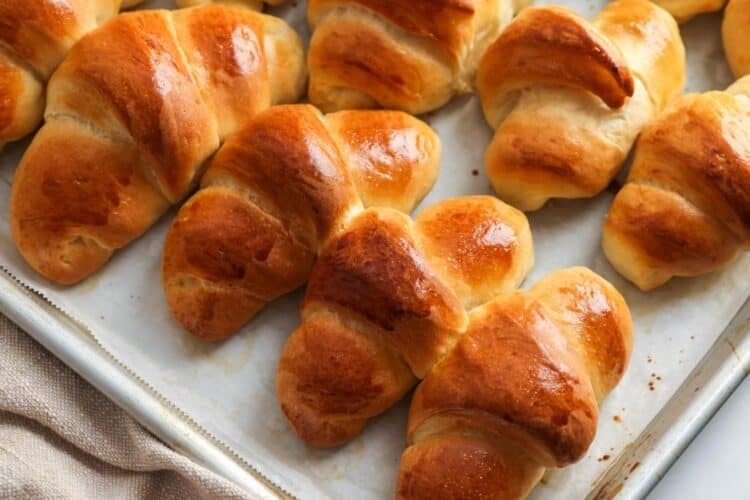 crescent rolls baked on a parchment lined baking sheet. They are browned and brushed with butter.