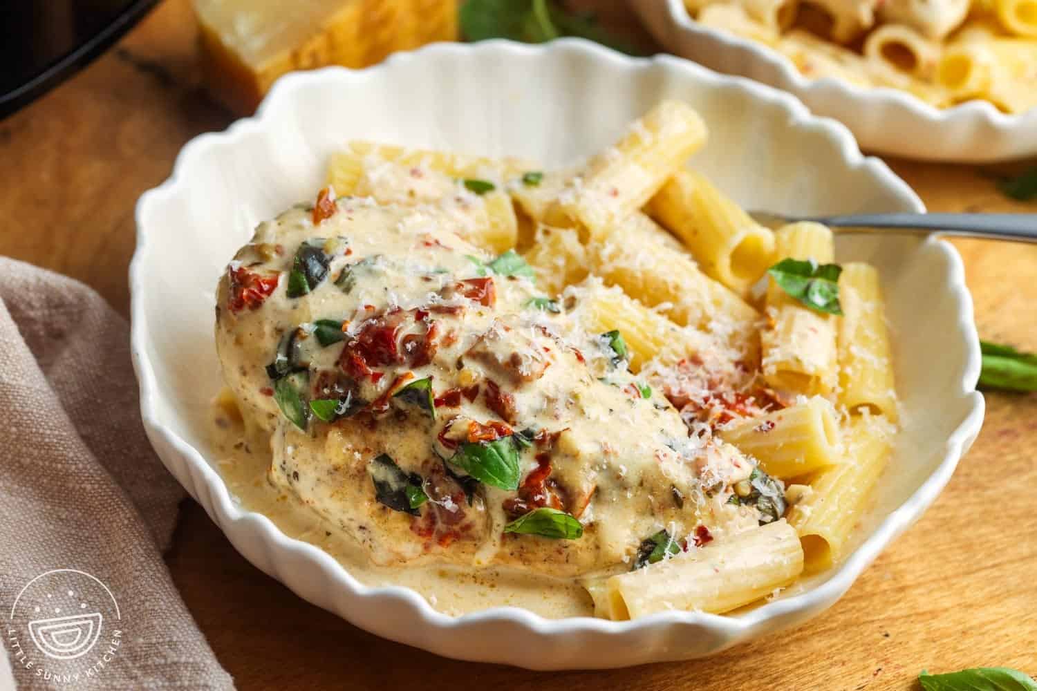 a bowl of pasta with a whole chicken breast. The chicken breast is cooked "marry me" style in a creamy sundried tomato sauce.
