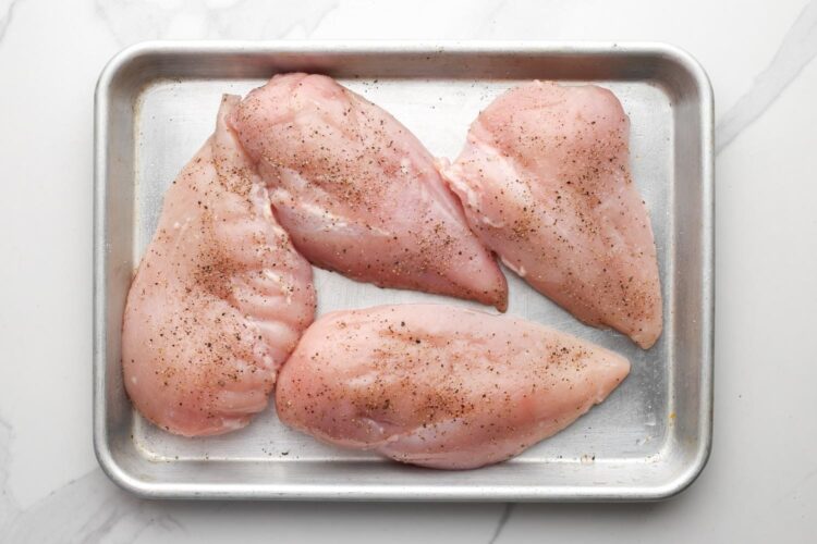 four chicken breasts on a small pan, seasoned with salt and pepper.