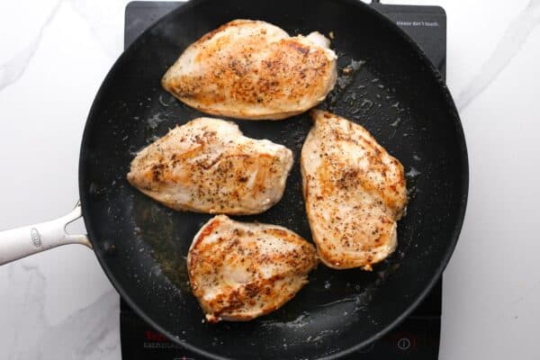 four chicken breasts searing in a nonstick skillet.