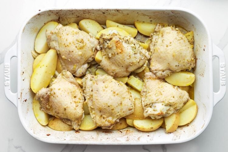 partially cooked chicken thighs on top of roasted potatoes