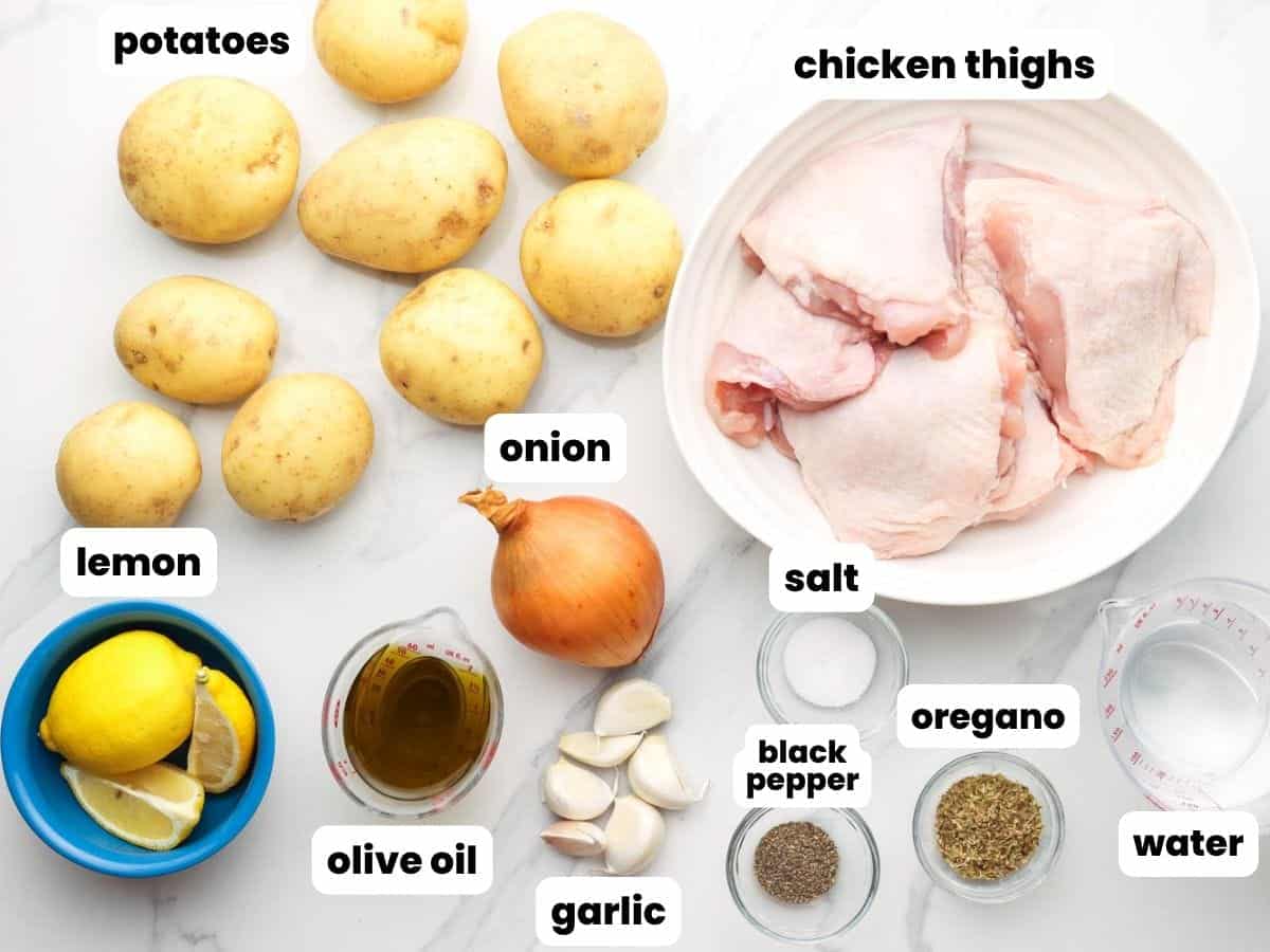 a plate of raw chicken thighs next to potatoes, lemon, and seasonings.