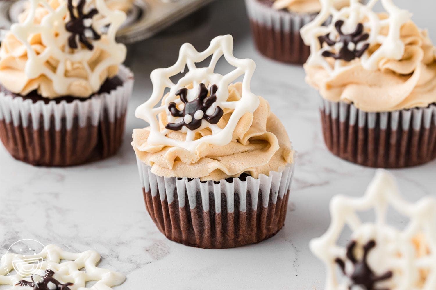 Chocolate and peanut butter cupcakes decorated with piped white chocolate spider webs and candy spiders for Halloween.