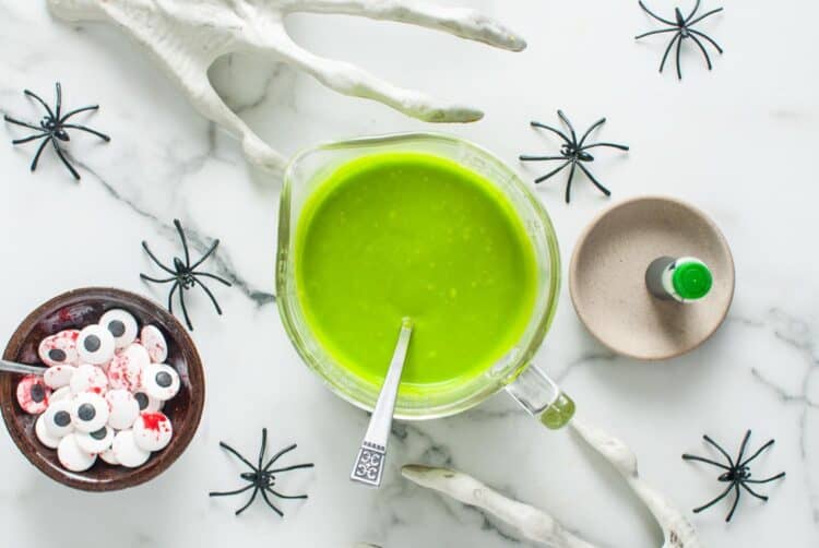 A small bowl of bright green hollandaise sauce with candy eyeballs nearby, ready for decorating.