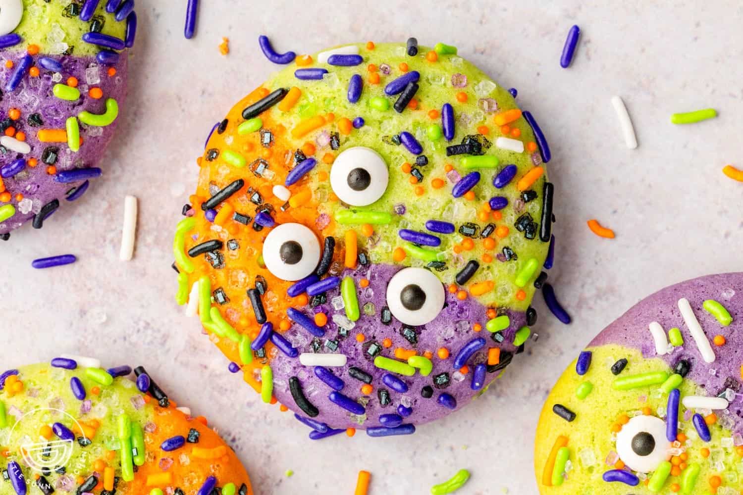 Brightly colored Halloween cookie decorated in orange, green, purple, and yellow with candy eyeballs and festive sprinkles.