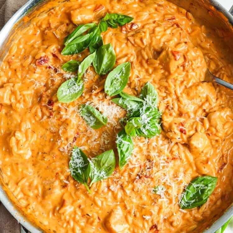 overhead view of a large skillet filled with creamy, tomatoey orzo with chicken and sundried tomatoes.