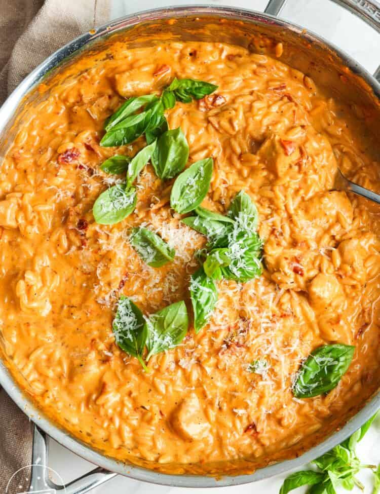 overhead view of a large skillet filled with creamy, tomatoey orzo with chicken and sundried tomatoes.