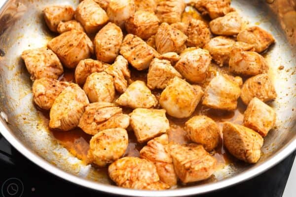 diced chicken breast cooking in a skillet with oil from sundried tomatoes.