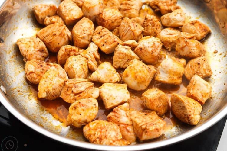 diced chicken breast cooking in a skillet with oil from sundried tomatoes.