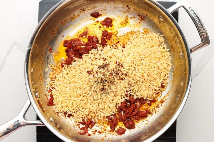 dried orzo and seasonings added to a skillet with sundried tomatoes.