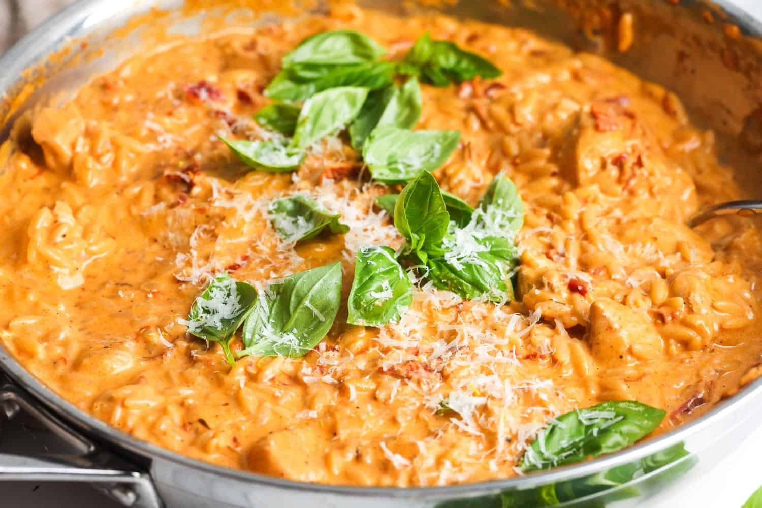 closeup of a skillet of one pan marry me orzo with chicken, garnished with parmesan and basil leaves.