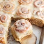 a sheet pan of mini cinnamon rolls. A small silver spatula is lifting one roll away from the rest.
