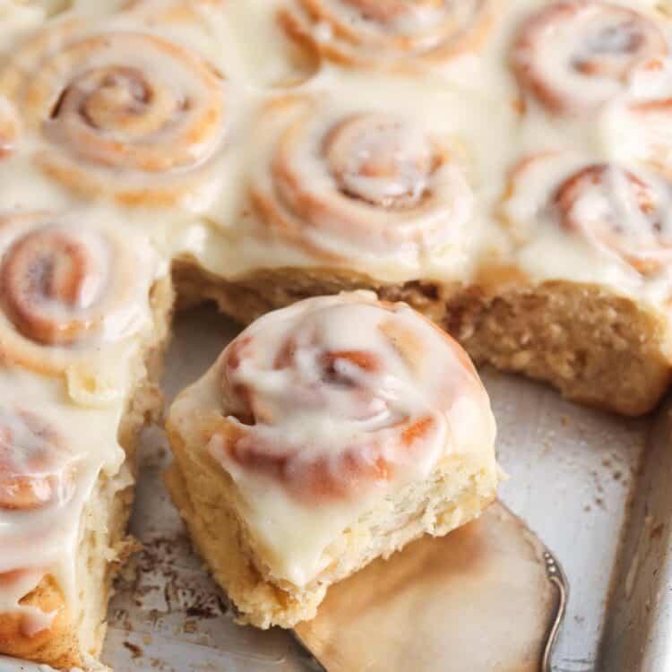 a sheet pan of mini cinnamon rolls. A small silver spatula is lifting one roll away from the rest.