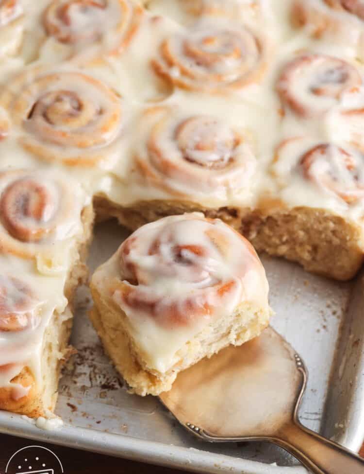 a sheet pan of mini cinnamon rolls. A small silver spatula is lifting one roll away from the rest.