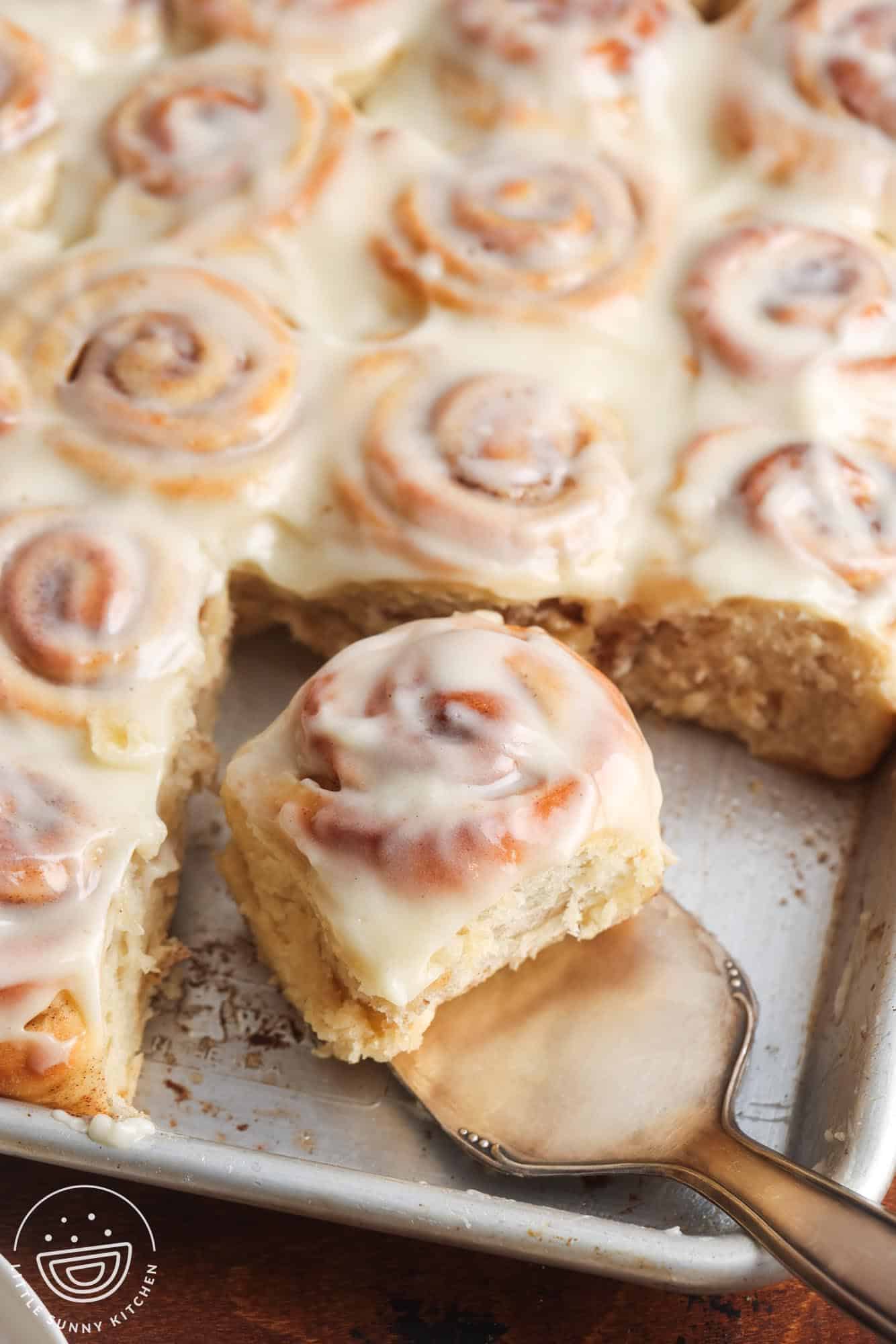 a sheet pan of mini cinnamon rolls. A small silver spatula is lifting one roll away from the rest.
